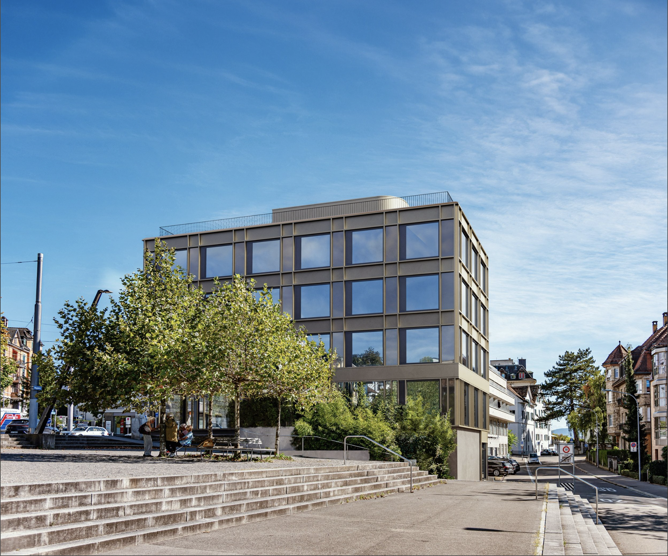 Modern office building with glass facade and trees in front.