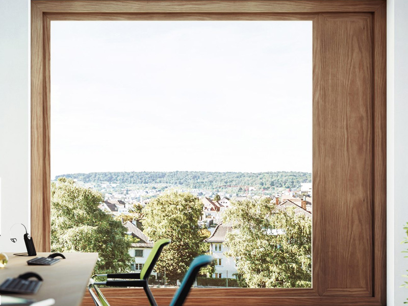 Office window with wooden frame and view of greenery and rooftops.